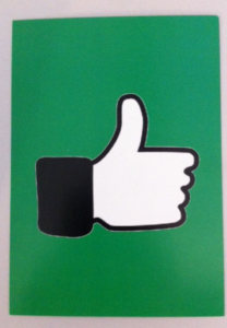Eine grüne Karte, auf der eine schwarz-weiße Hand zu sehen ist. Der Daumen zeigt nach oben